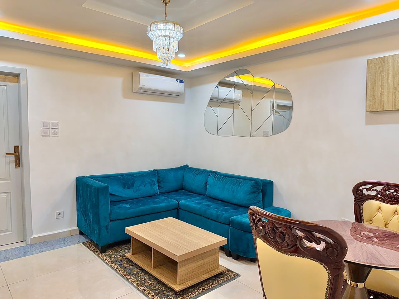 Un salon moderne avec un canapé d’angle bleu, une table basse en bois et une table à manger avec des chaises.