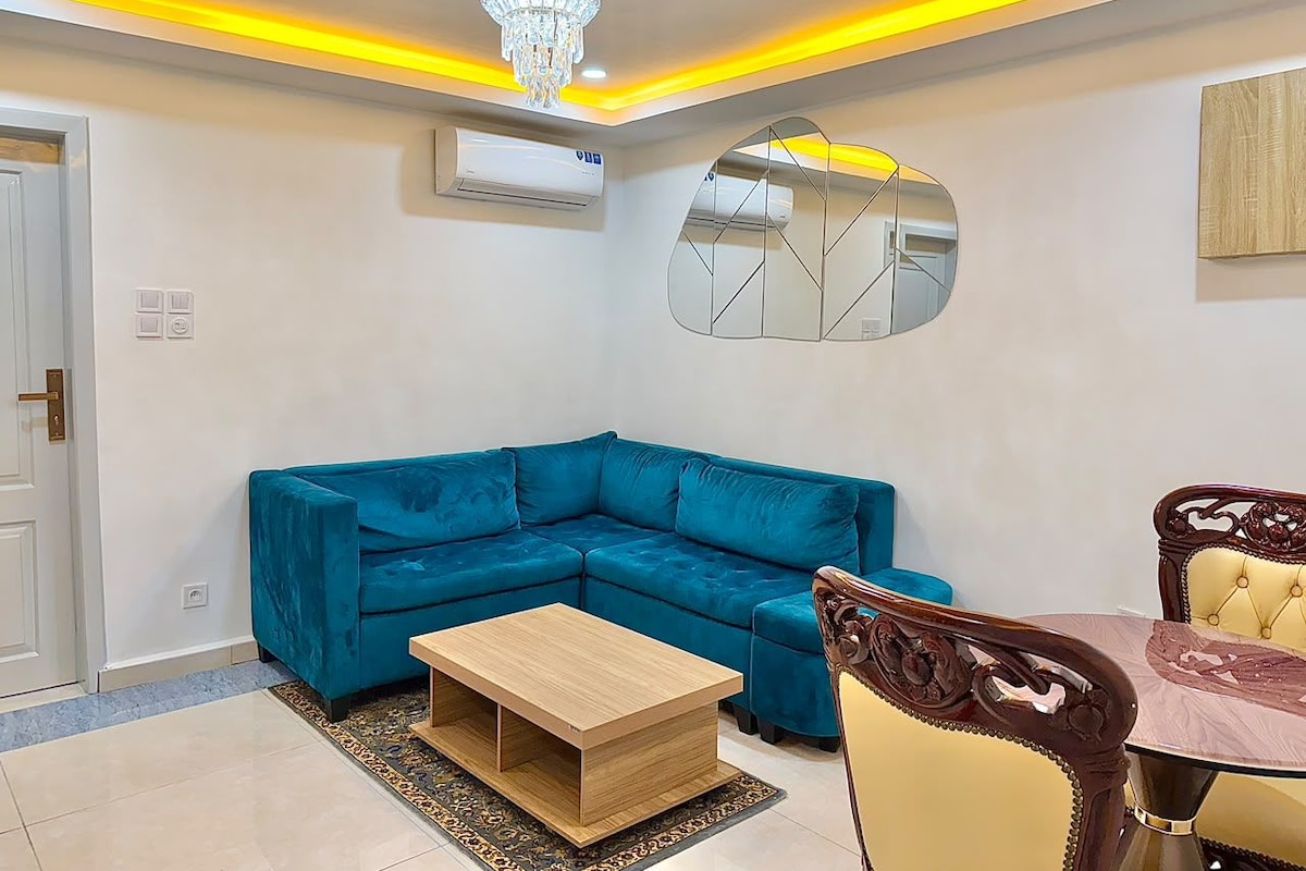 Een moderne woonkamer met een blauwe modulaire bank, een houten salontafel en een eettafel met stoelen.