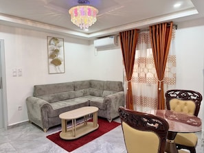 A living room with a sofa, a coffee table, and a dining table with chairs. - Residence la Marina Logpom (Douala)