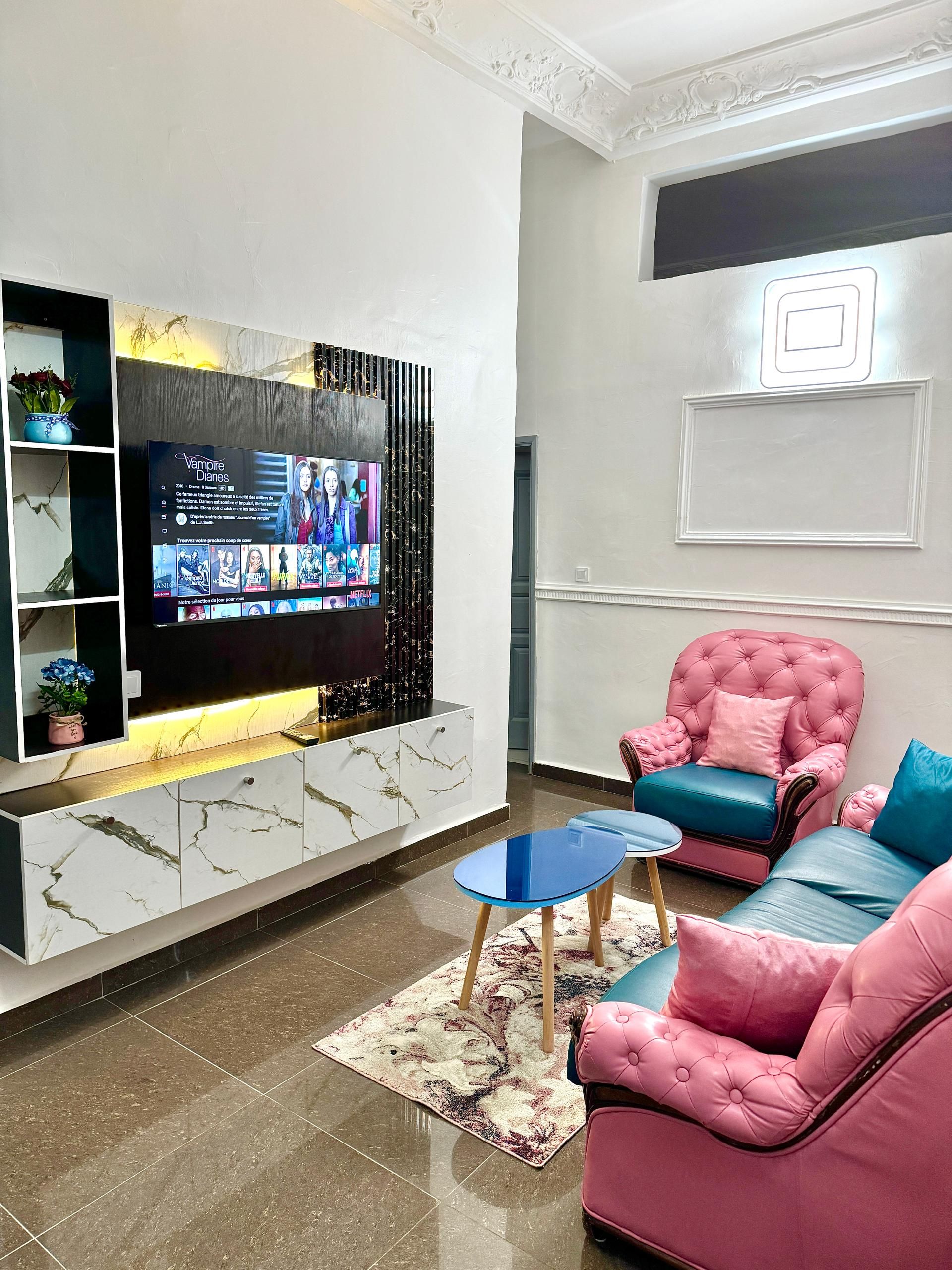 Un salon moderne avec un téléviseur à écran plat, un meuble en marbre, un canapé rose et une table basse bleue.