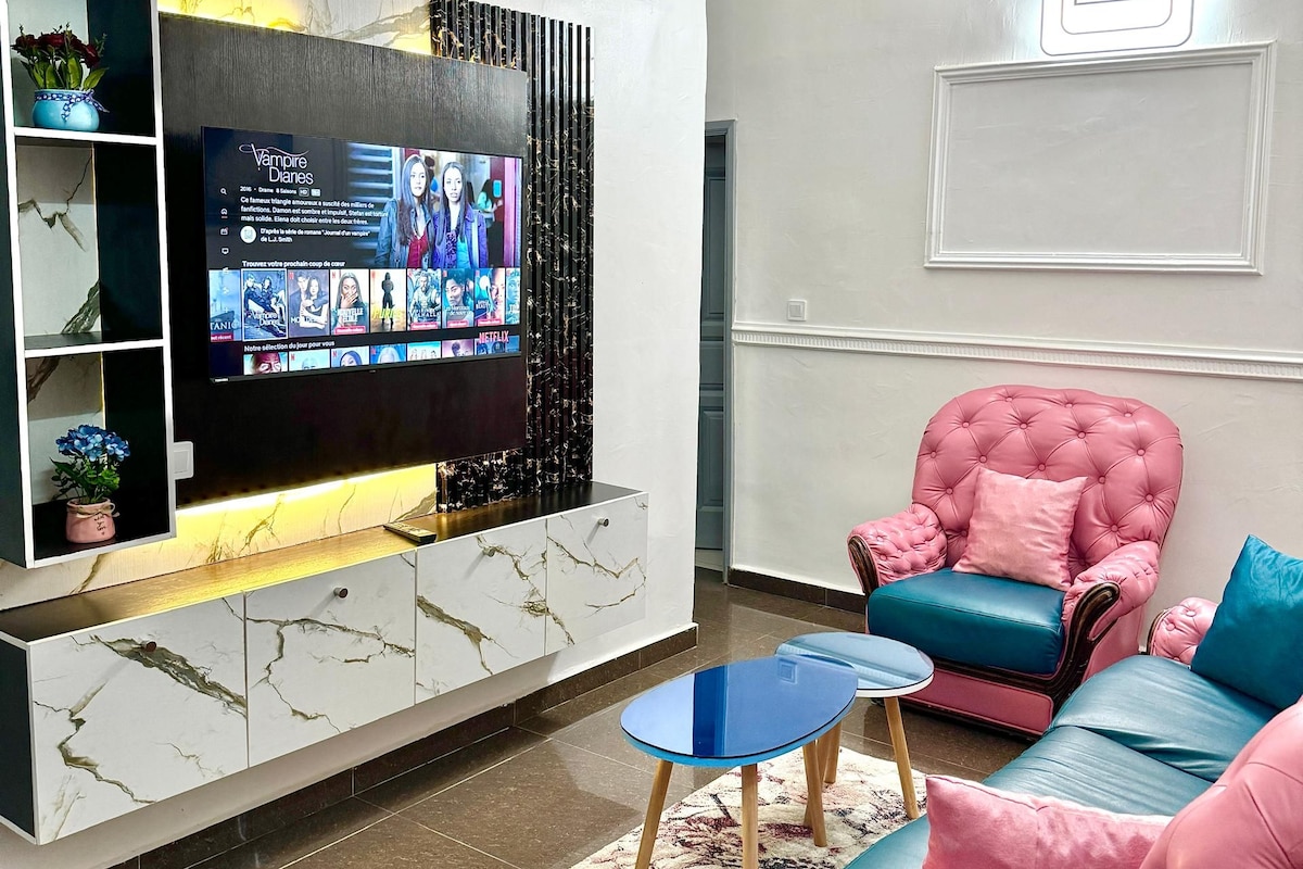 Een moderne woonkamer met een flatscreen televisie, een marmeren kast, een roze bank en een blauwe salontafel.