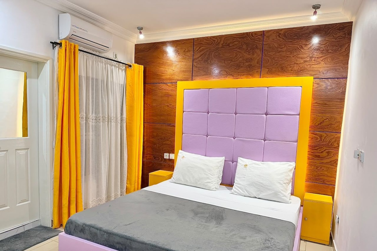 Een slaapkamer met een bed, gordijnen, een airconditioning en een houten wandpaneel.