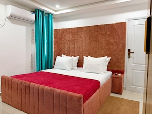 A hotel room with a large bed, a bedside table, an air conditioning unit, and a door. - Residence la Marina Logpom (Douala)