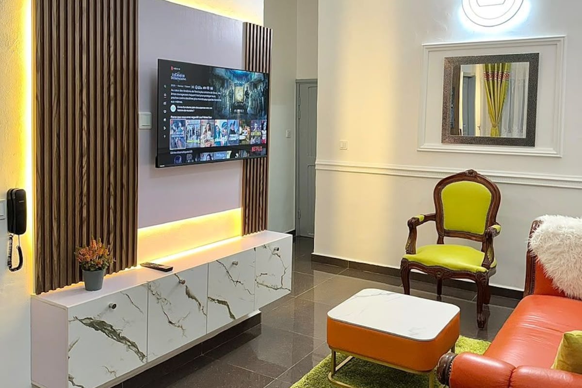 Een moderne woonkamer met een flatscreen televisie, een houten kast, een groen tapijt, een rode leren bank en een houten stoel.
