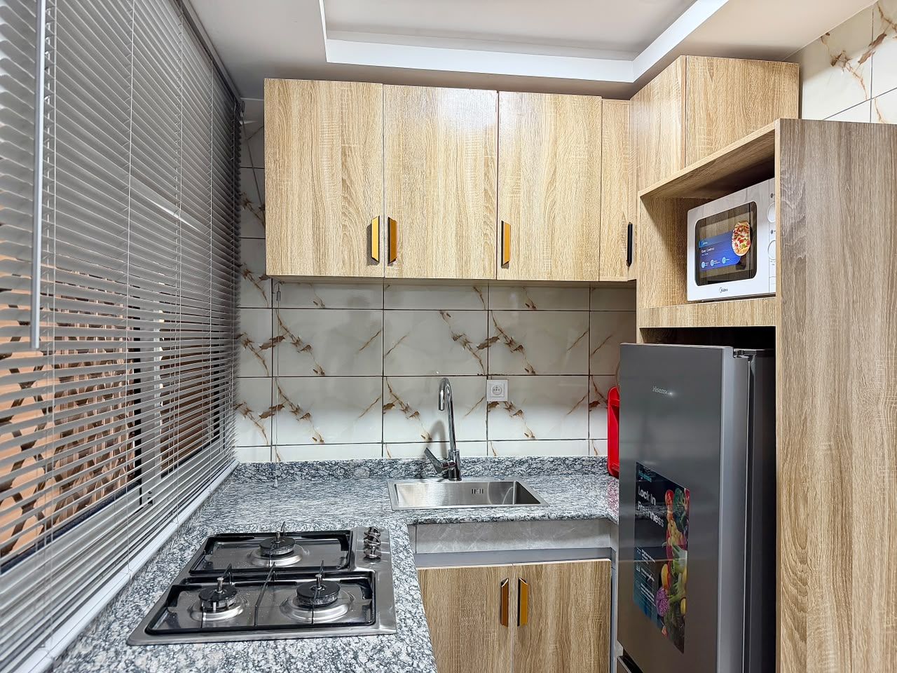 Una cocina con armarios de madera, un lavamanos de acero inoxidable, una estufa a gas y un refrigerador con pantalla digital.