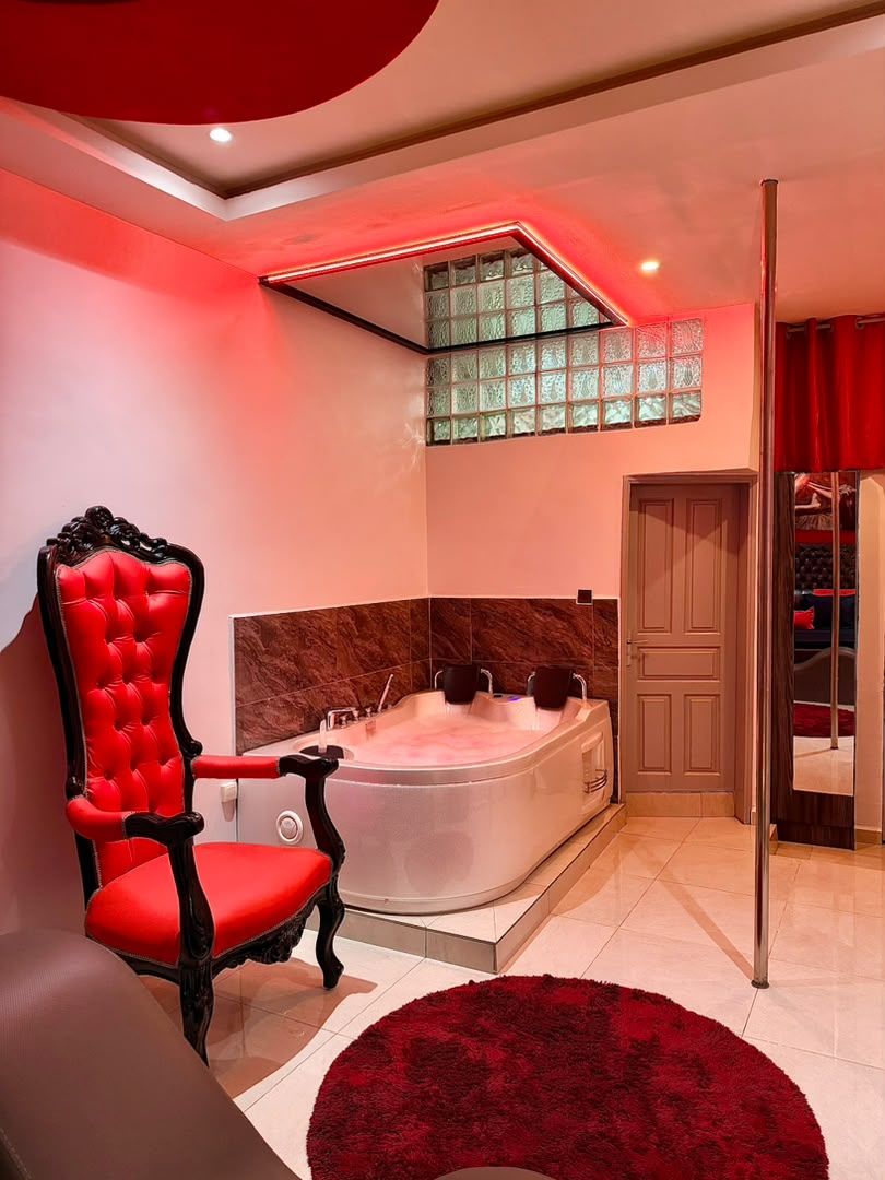A modern bathroom with a large bathtub, a red upholstered chair, and a red rug.
