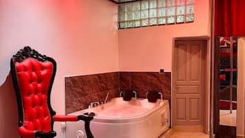 A modern bathroom with a large bathtub, a red upholstered chair, and a red rug.