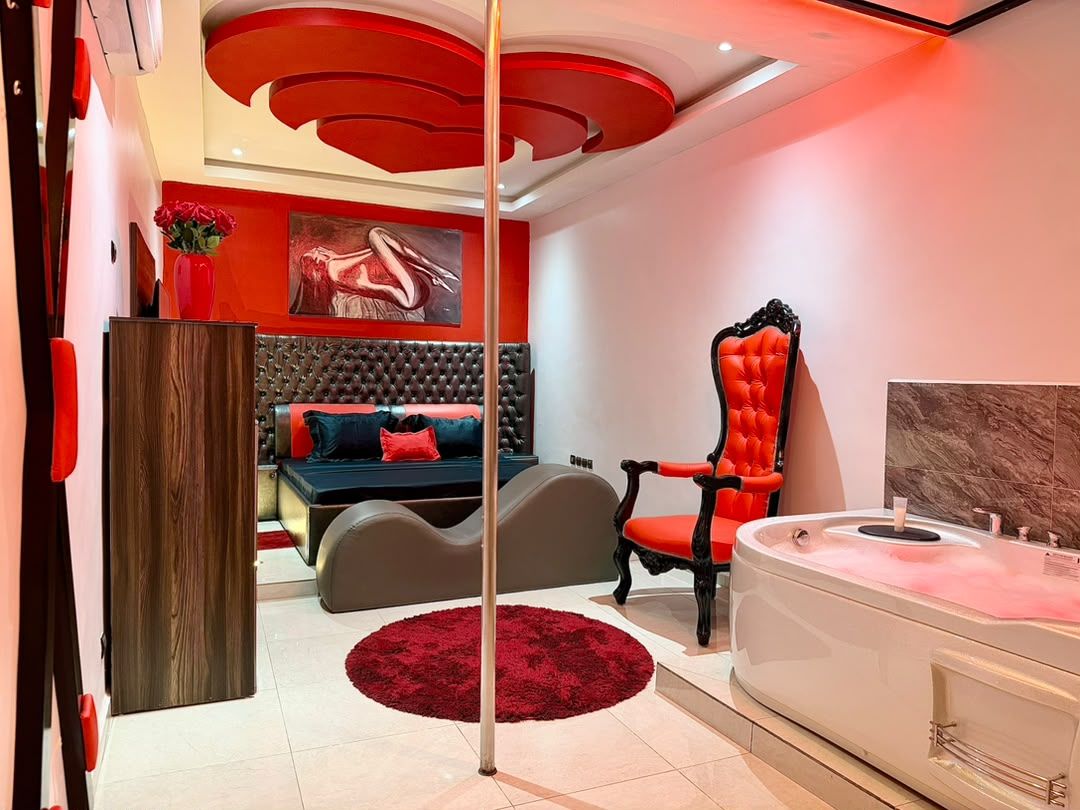 A modern bedroom with a large bed, a red accent chair, a white bathtub, and a red rug.