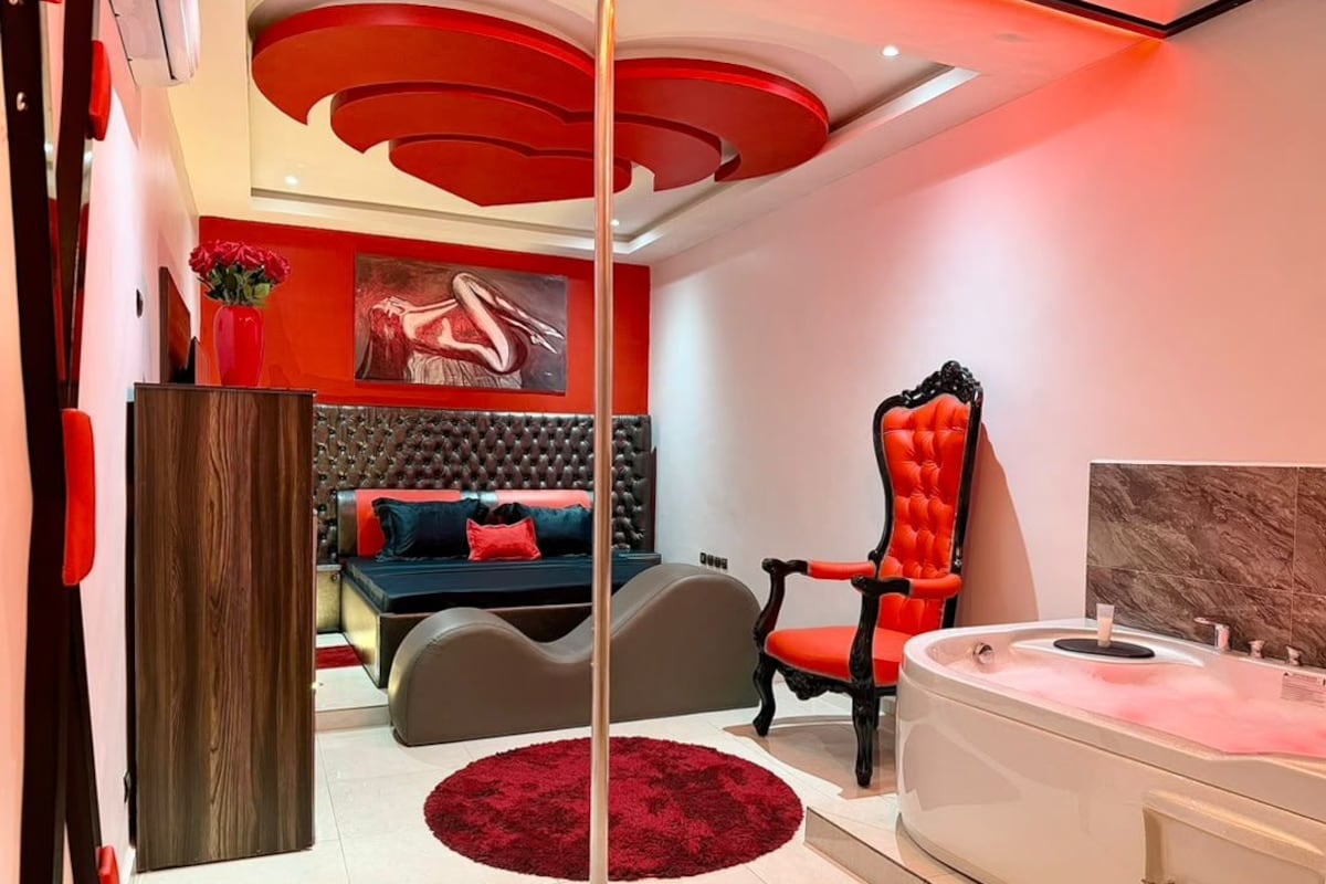 Een moderne slaapkamer met een groot bed, een rode fauteuil, een witte badkuip en een rood vloerkleed.