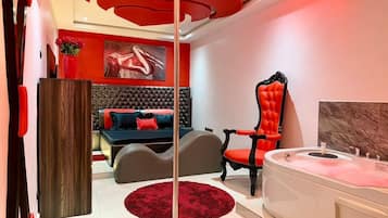 A modern bedroom with a large bed, a red accent chair, a white bathtub, and a red rug.