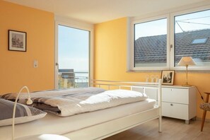 A bedroom with a bed, bedside table, lamp, and a window with a view of a building. - Holiday apartment with 2 bedrooms (Überlingen)