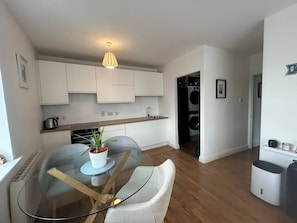 A modern kitchen with white cabinets, a glass dining table with a potted plant, and a washing machine in the background. - Stylish 2BDR Apt with Free parking in Dublin 8 (Dublin)
