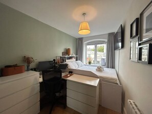 A compact bedroom with a bed, desk, chair, and a window with curtains. - Stylish 2BDR Apt with Free parking in Dublin 8 (Dublin)