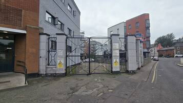 A gated entrance to a building with CCTV warning signs, a pedestrian pathway, and parked cars.