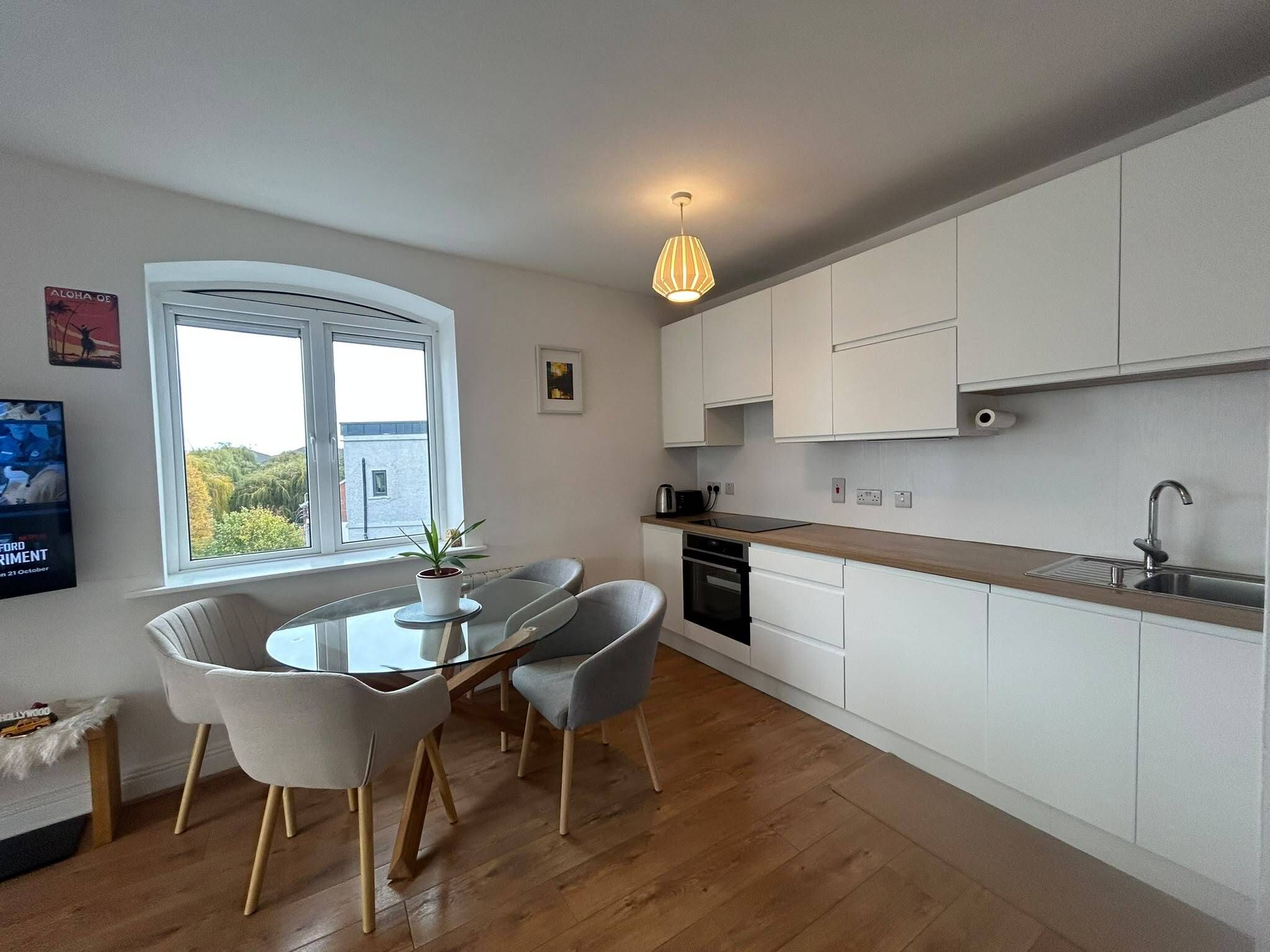 A modern kitchen with white cabinets, a dining area with a glass table and chairs, and a view through the window.
