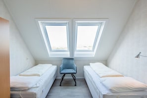 Une petite pièce unique comprenant deux lits, une chaise et une lucarne.