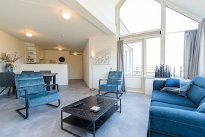 A modern living room with a sofa, two armchairs, a coffee table, and a dining area in the background. - Holiday apartment in Nes with swimming pool (Nes)