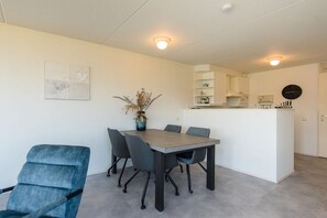 A modern kitchen with white cabinets and a central island, a dining area with a table and chairs, and a small decorative plant. - Holiday apartment in Nes with swimming pool (Nes)
