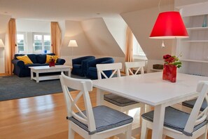 A modern living room with a white dining table, blue and white chairs, a blue sofa with yellow cushions, and a red lamp. - Holiday apartment with 2 bedrooms (Süddorf)