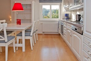 Une cuisine avec des meubles blancs, une fenêtre, une lampe rouge et une table avec des chaises.