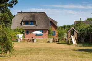 A house with a thatched roof, a brick lower section, and a small wooden playhouse with a slide. - Holiday apartment with 2 bedrooms (Süddorf)