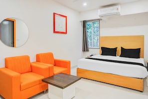 A hotel room with a bed, a sofa, a small table, a mirror, and a window with a view of trees. - Townhouse Hadapsar (Pune)