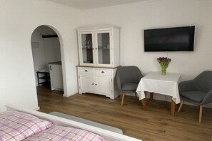 A bedroom with a bed, a white cabinet, a TV, and a small table with a vase. - Apartment with 1 bedroom (Berchtesgaden)