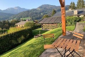 A patio with a wooden bench and a chair, overlooking a lush green landscape with mountains in the background. - Apartment with 1 bedroom (Berchtesgaden)