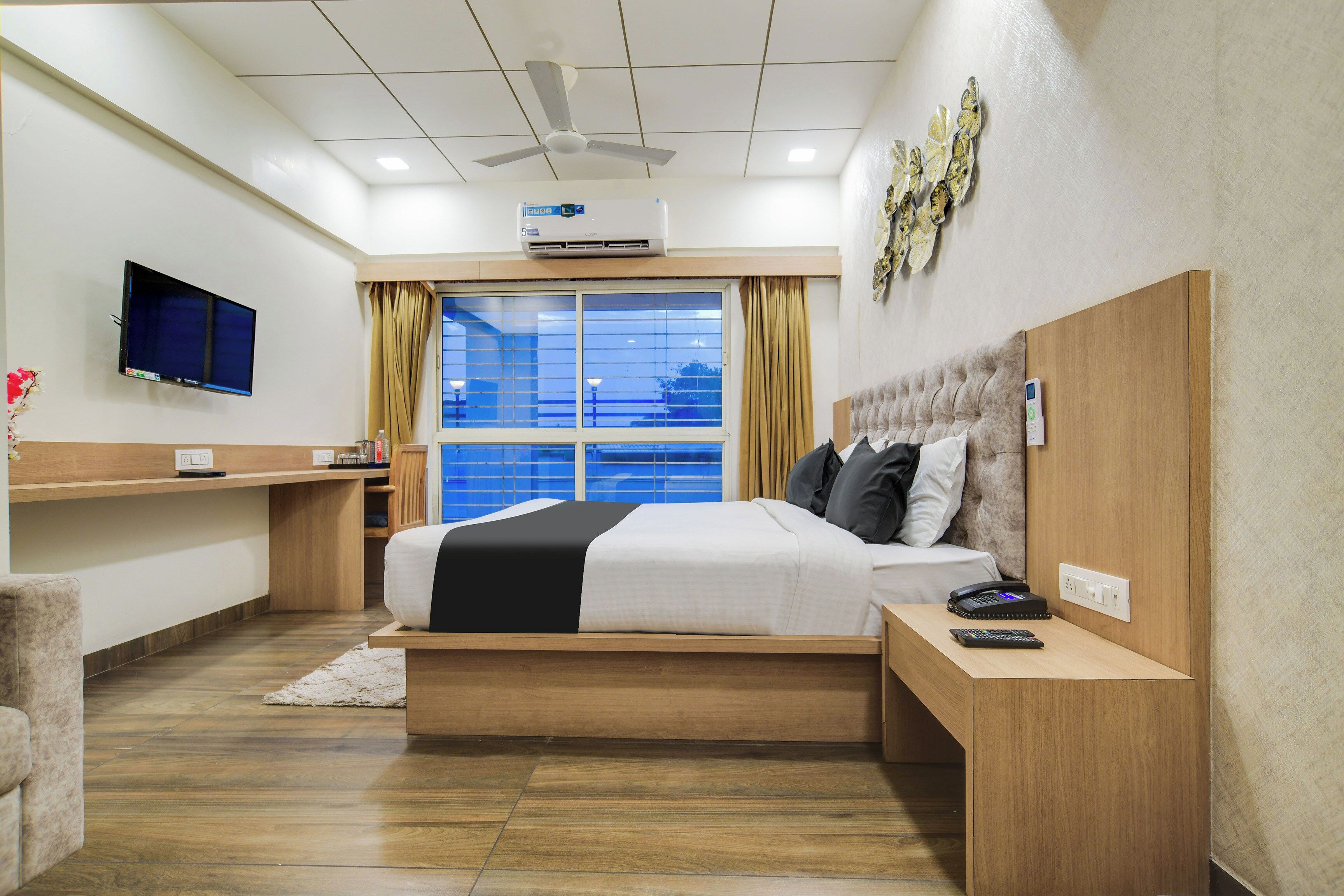 A hotel room with a bed, bedside table, TV, air conditioning unit, and a window with curtains.