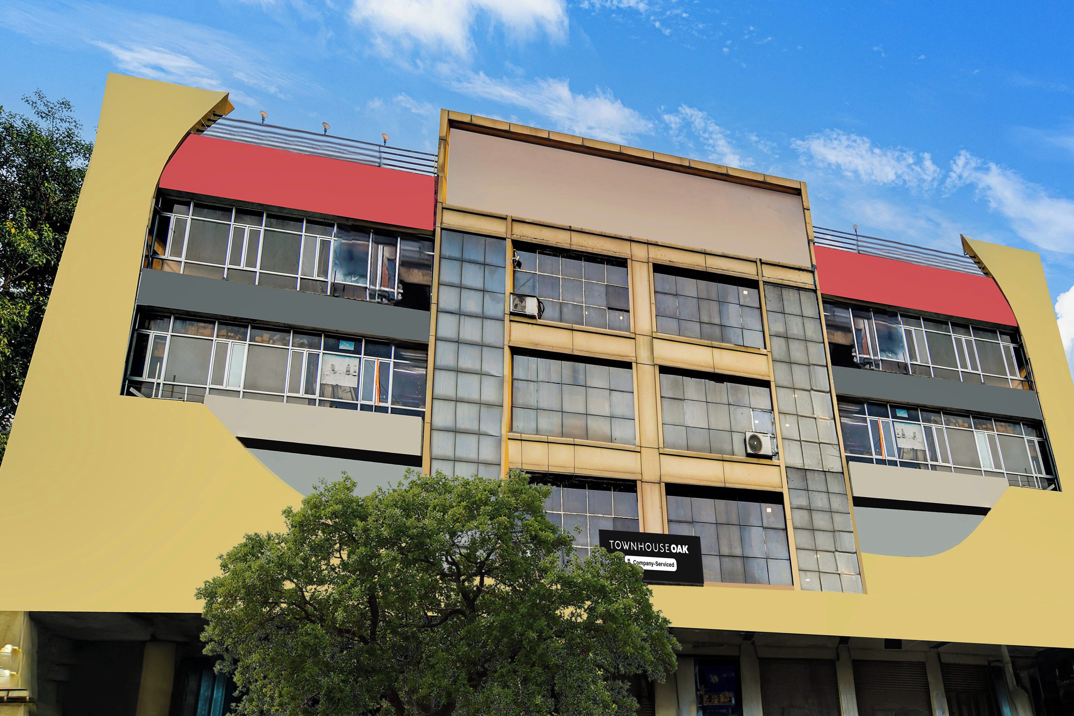 A multi-story building with a yellow facade, red accents, and a sign indicating it is a company-serviced townhouse.