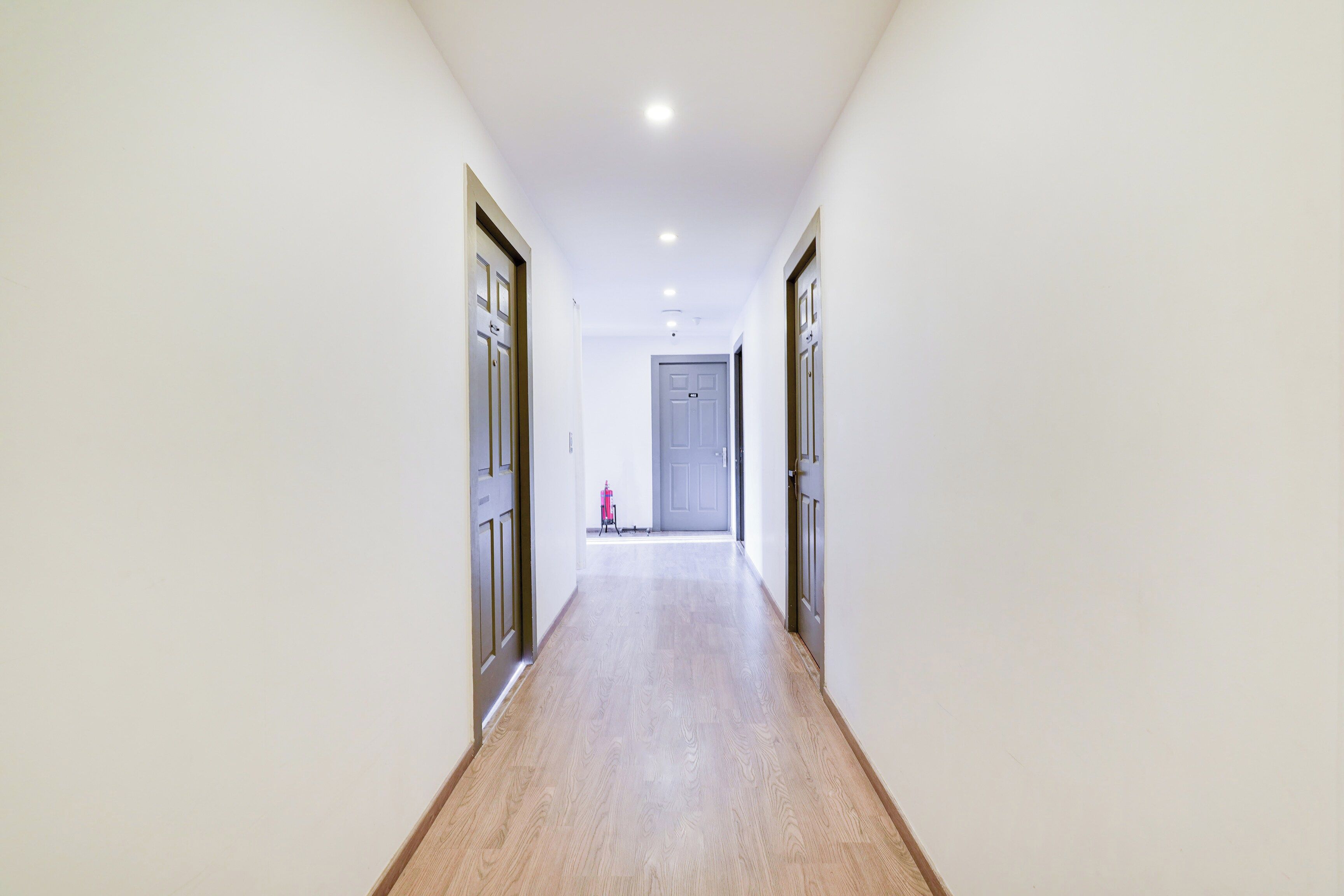 Un pasillo con piso de madera, paredes blancas y puertas a ambos lados.