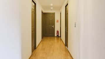 Un pasillo estrecho con suelo de madera, puertas a ambos lados y un extintor fijado en la pared.