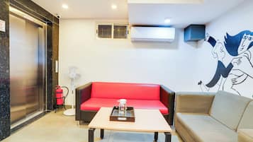 Una sala de estar moderna con un sofá rojo, un sofá gris, una mesa de centro, un aire acondicionado instalado en la pared y un extintor.