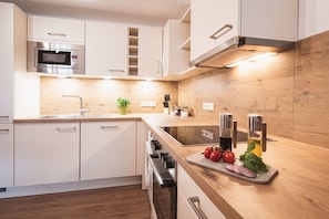 A modern kitchen with white cabinetry, a built-in microwave, a stainless steel range hood, and a wooden countertop with a cutting board and fresh vegetables. - Holiday apartment with 1 bedroom (Rettenberg)