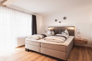 Een moderne slaapkamer met een groot bed, nachtkastjes en een raam met gordijnen.