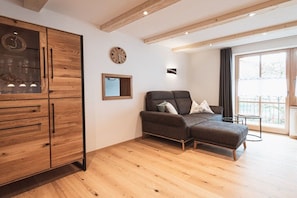 A modern living room with a sofa, wooden cabinet, and a large window. - Holiday apartment with 1 bedroom (Rettenberg)