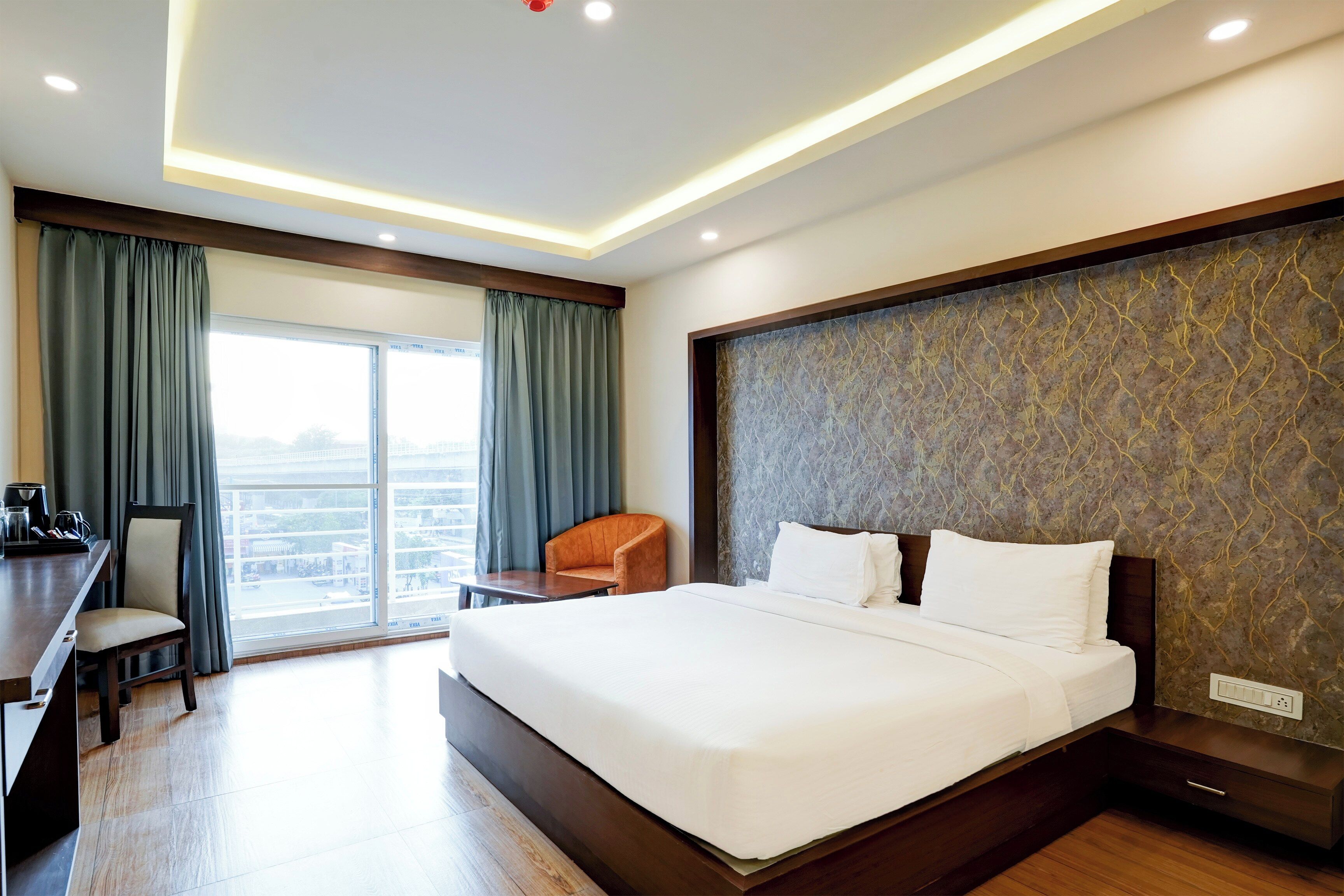 A hotel room with a large bed, a desk, a chair, and a view of the city through the window.