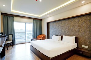 A hotel room with a large bed, a desk, a chair, and a view of the city through the window.