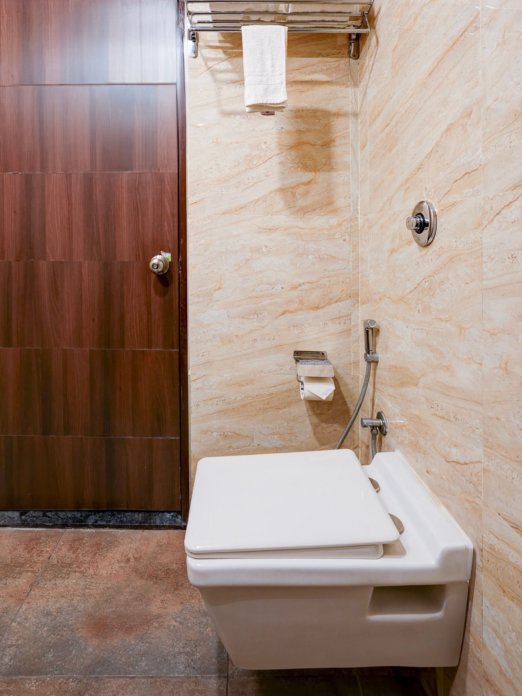 Un baño con puerta de madera, un lavamanos blanco con toallero encima y una zona de ducha.