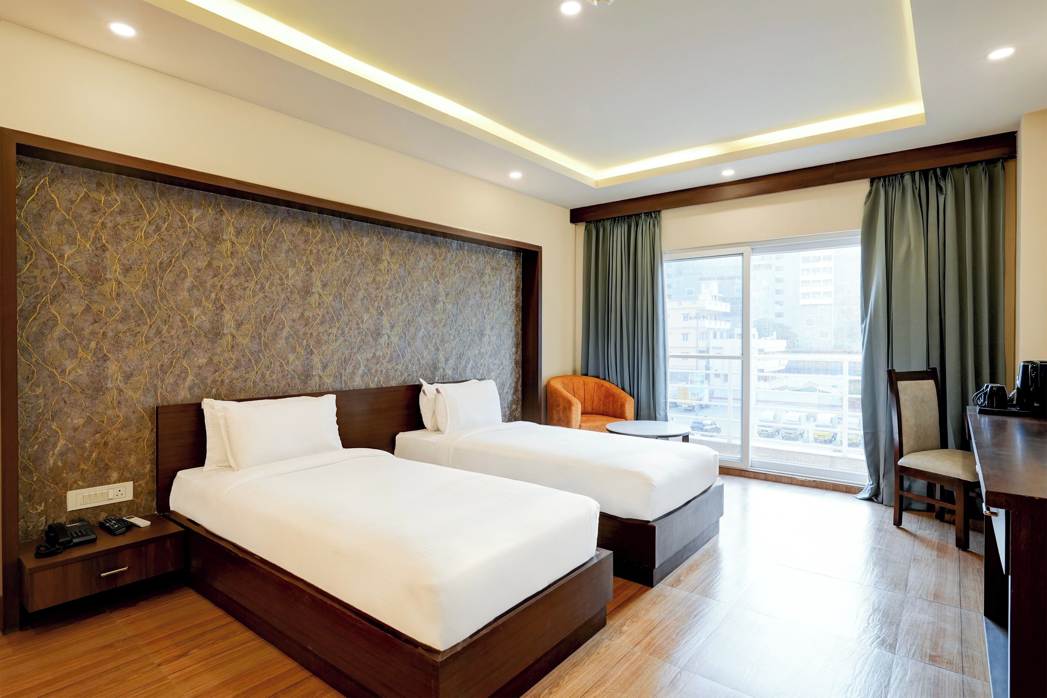A hotel room with two beds, a desk, a chair, and a view of the city.