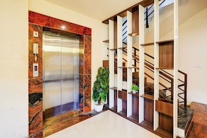 An elevator with a marble finish, a staircase with wooden railings, and a potted plant.