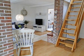 A living room with a television, a white cabinet, a brick wall, and a wooden ladder. - Föh's little house || Kappeln Stadt (Kappeln Stadt)