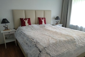 A bed with a fluffy white cover, two red pillows with deer designs, a beige headboard, and two bedside tables with lamps. - Your dream home "Fichtelzauber" (Mehlmeisel)