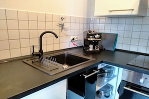 A kitchen with a black countertop, a sink with a faucet, a coffee machine, and a stove. - Your dream home "Fichtelzauber" (Mehlmeisel)