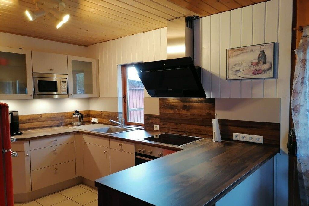 A modern kitchen with wooden cabinets, a stainless steel microwave, a black range hood, and a painting on the wall.