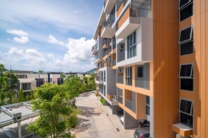 Un edificio residencial de varios pisos con balcones, cielo despejado y una calle bordeada de árboles.