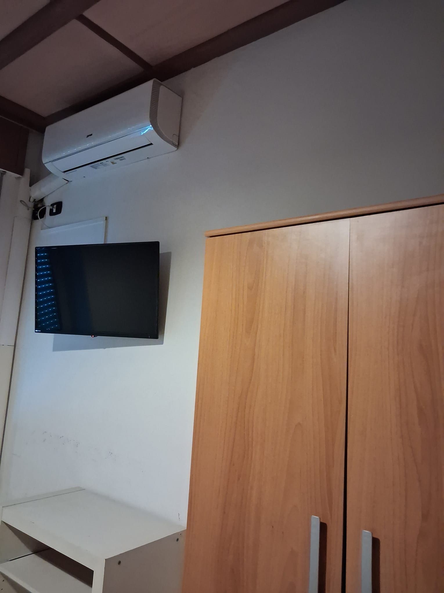 Une pièce avec un mur blanc, une armoire en bois et un téléviseur à écran plat fixé au-dessus.