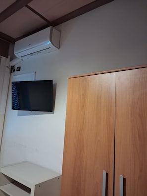 A room with a white wall, a wooden wardrobe, and a flat-screen TV mounted above it. - Don Carlos (Buscate)
