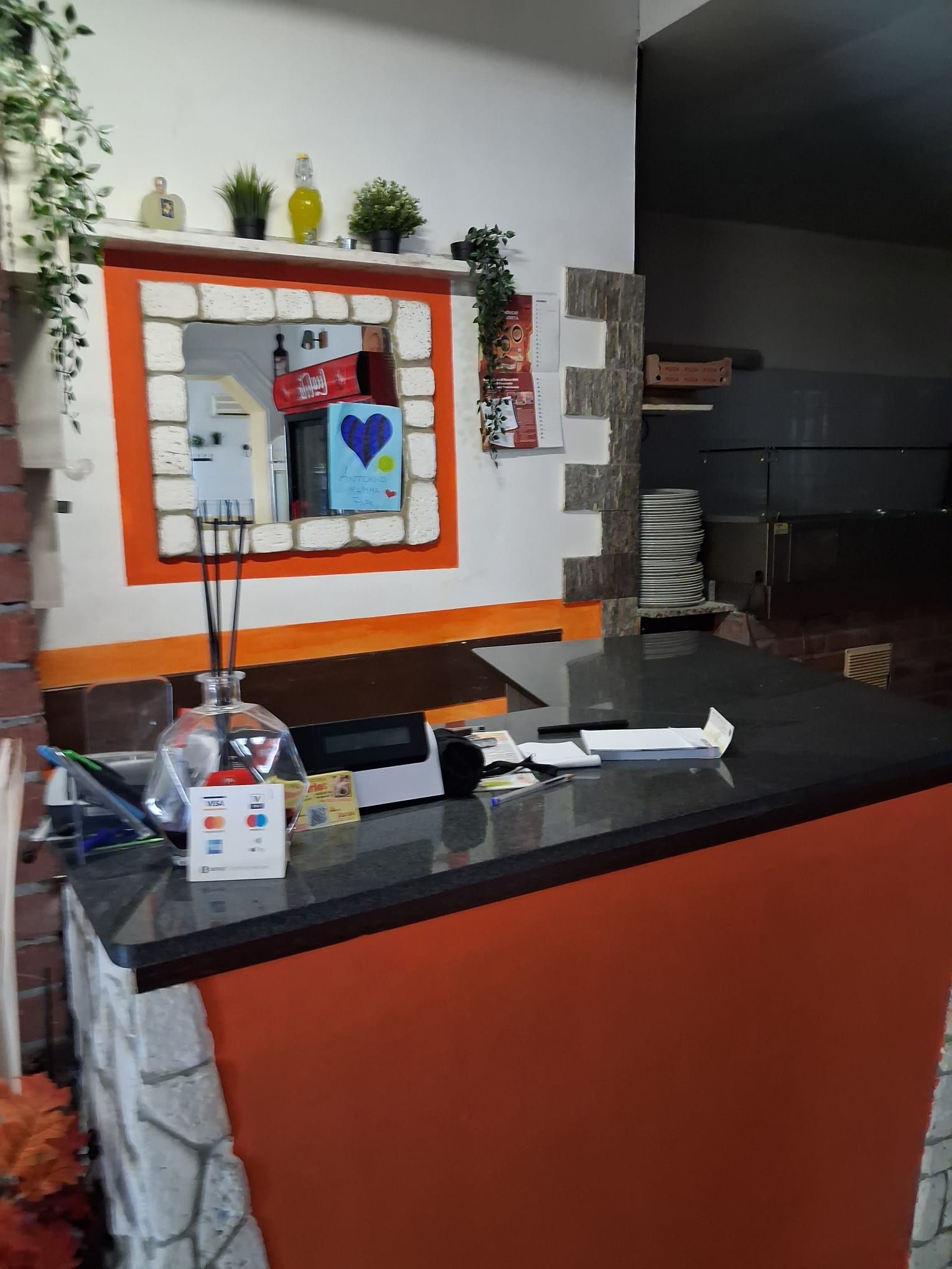 A reception area with a counter, a Coca-Cola refrigerator, a Visa card machine, and a decorative heart sign.