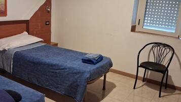 Une chambre avec deux lits simples, une chaise et une fenêtre avec des stores.